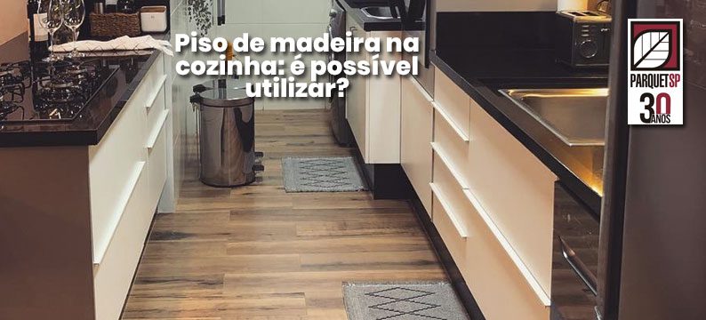 Ao fundo da imagem, há uma cozinha com piso de madeira.