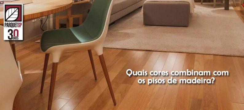 Ao fundo da imagem, há uma sala de estar com sofá, tapete, mesa, cadeira e piso de madeira.