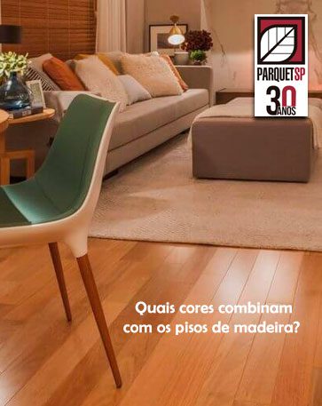 Ao fundo da imagem, há uma sala de estar com sofá, tapete, mesa, cadeira e piso de madeira.