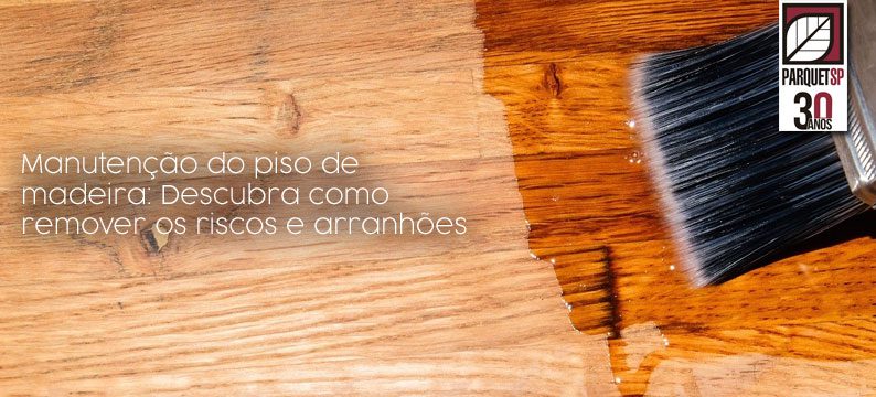 A imagem mostra um piso de madeira com uma parte feita sem manutenção e outra com, e um pincel em cima da parte com manutenção.
