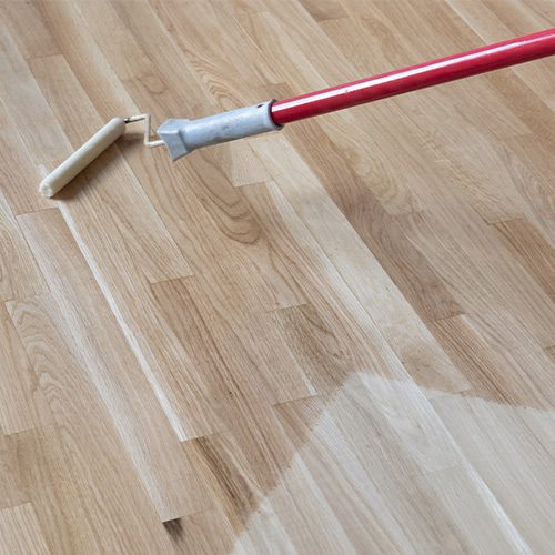 Na imagem um rolo passando verniz em um piso de madeira