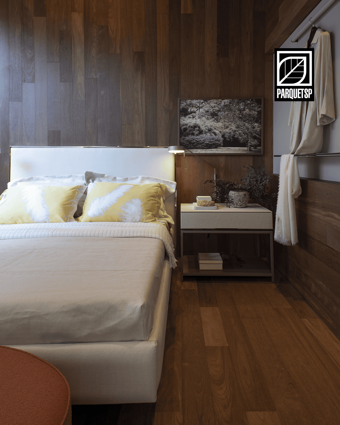 Quarto aconchegante com piso e parede de madeira, cama de cabeceira clara com almofadas amarelas e abajur moderno, transmitindo conforto e elegância.