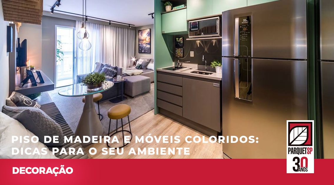 Ao fundo da imagem, há uma cozinha com móveis coloridos e o piso de madeira.