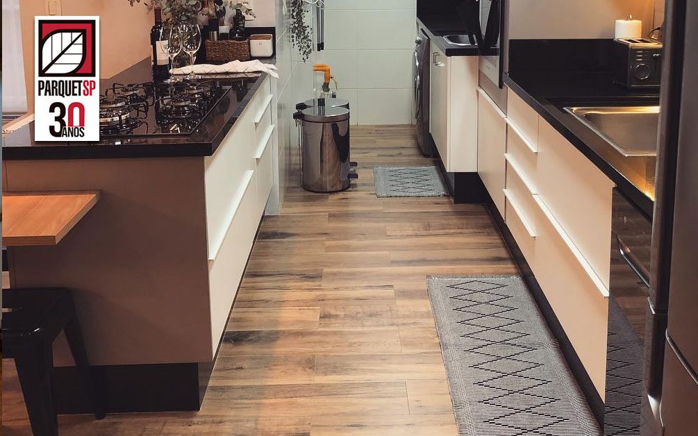 Ao fundo da imagem, há uma cozinha com piso de madeira.