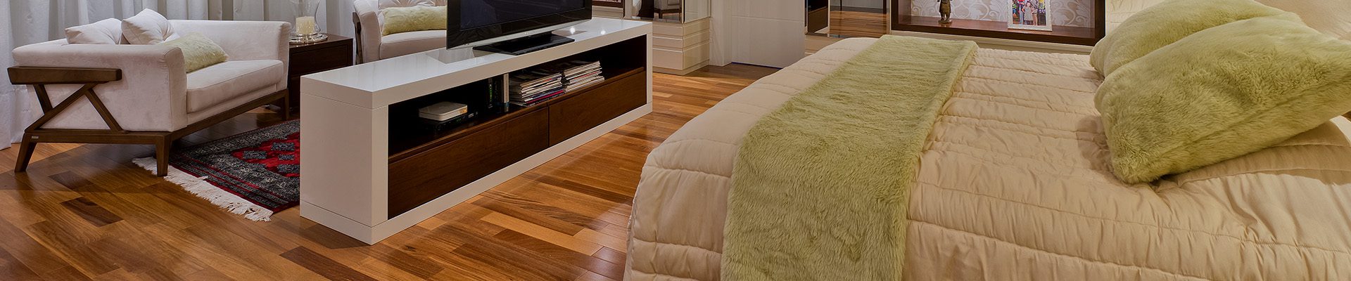 Quarto amplo com piso de madeira, cama de casal, TV em painel central, iluminação embutida e estantes decorativas ao fundo.