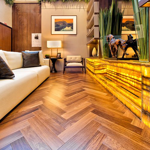Sala de estar elegante com piso de madeira em padrão espinha de peixe, sofá branco, decoração sofisticada e iluminação suave, criando um ambiente aconchegante e moderno.