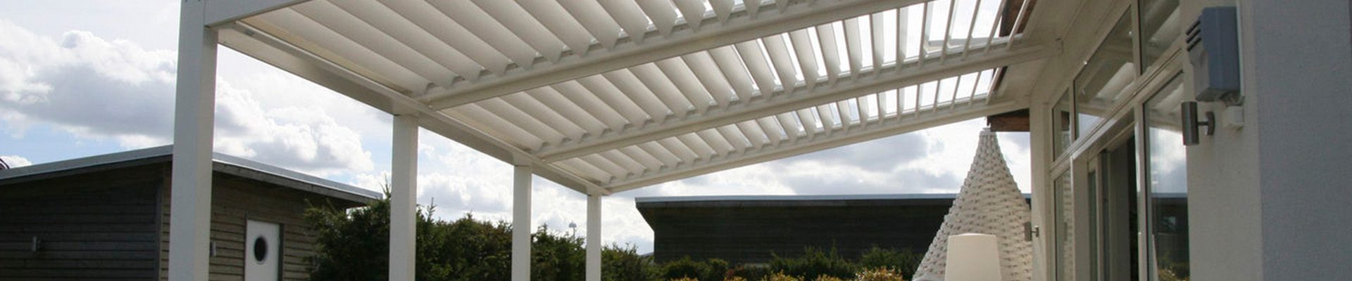 Área externa com pergolado de madeira branco, móveis de jardim e iluminação natural criando um ambiente aconchegante e moderno.