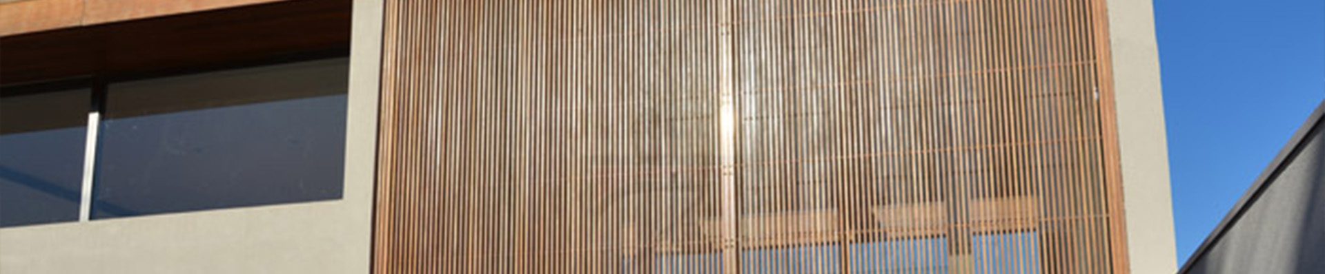 A imagem mostra a fachada de uma casa moderna com brises de madeira verticais cobrindo uma grande janela de vidro, proporcionando estética e funcionalidade.