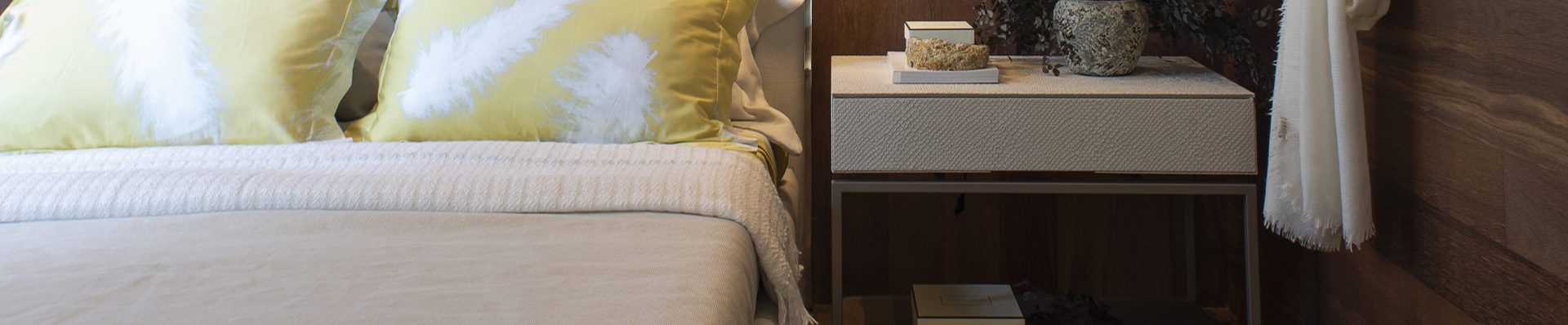 Quarto aconchegante com piso e parede de madeira, cama de cabeceira clara com almofadas amarelas e abajur moderno, transmitindo conforto e elegância.