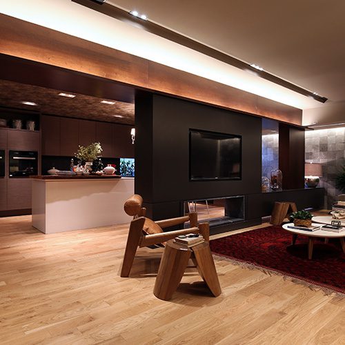 Sala moderna com piso de madeira clara, decoração aconchegante, móveis de design único, iluminação embutida e tapete vermelho, criando um ambiente sofisticado e acolhedor.