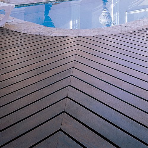 Imagem de um deck de madeira ao redor de uma piscina, com design em padrão geométrico. Ideal para destacar elegância e qualidade de materiais em áreas externas e piscinas.