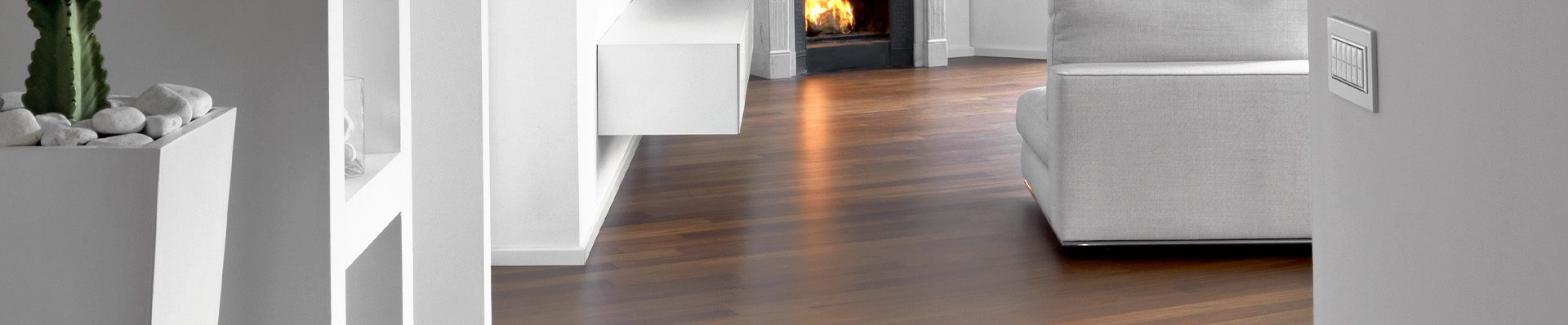 Imagem ilustra um piso de madeira, em destaque em uma sala com móveis brancos.