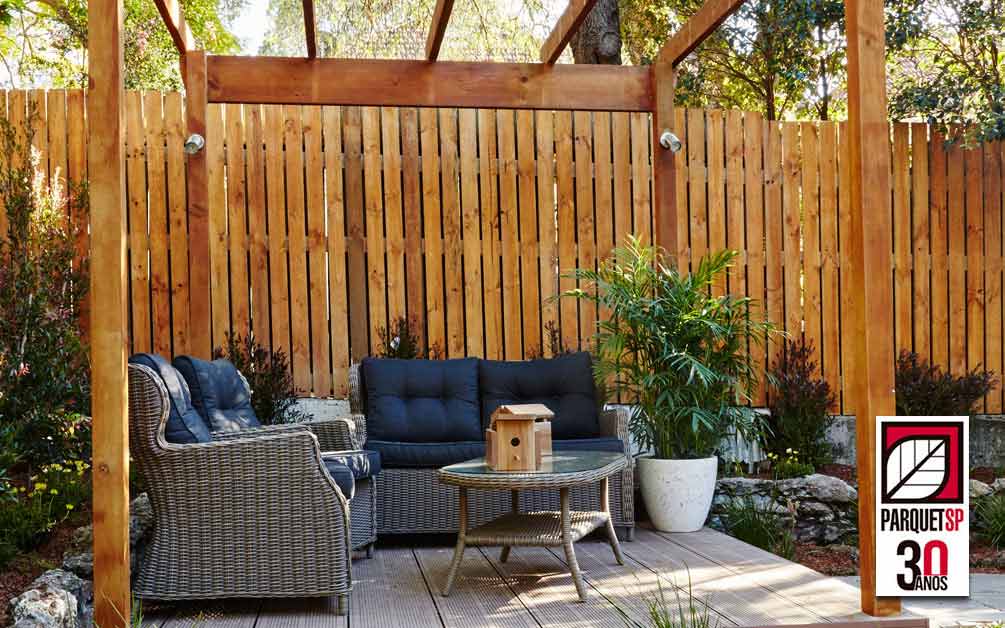 Jardim com sofás, mesa de certo, parede de deck de madeira e pergolado de madeira - ParquetSP