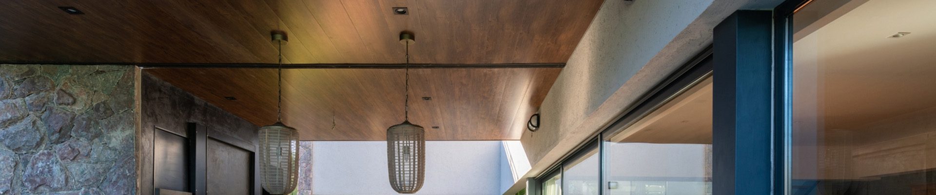 Área gourmet com mesa e bancos, teto em madeira, luminárias pendentes e portas de vidro integrando o ambiente ao espaço externo.