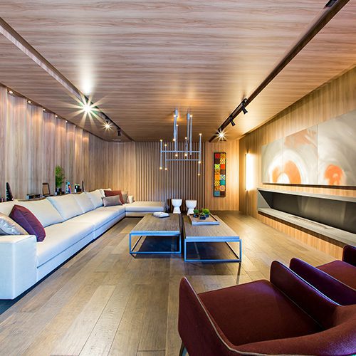 Sala de estar moderna com forro e piso de madeira, sofá branco, poltronas vinho e iluminação embutida, transmitindo sofisticação e aconchego.