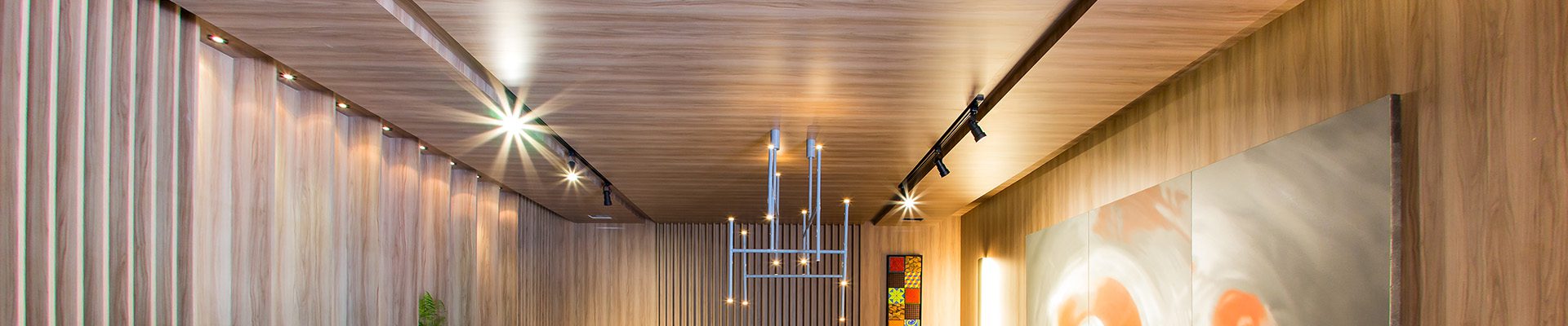 Sala de estar moderna com forro e piso de madeira, sofá branco, poltronas vinho e iluminação embutida, transmitindo sofisticação e aconchego.