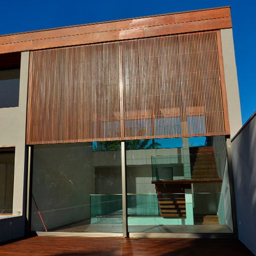 Fachada residencial contemporânea com brise de madeira vertical, grandes panos de vidro e integração entre áreas internas e externas.
