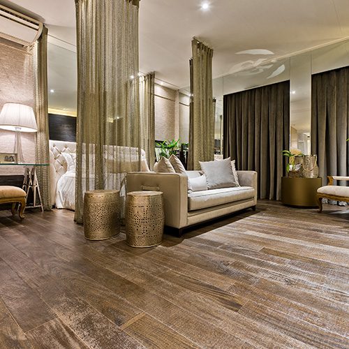 Sala sofisticada com piso de madeira escura, sofá bege, cortinas elegantes, espelhos nas paredes e iluminação suave.