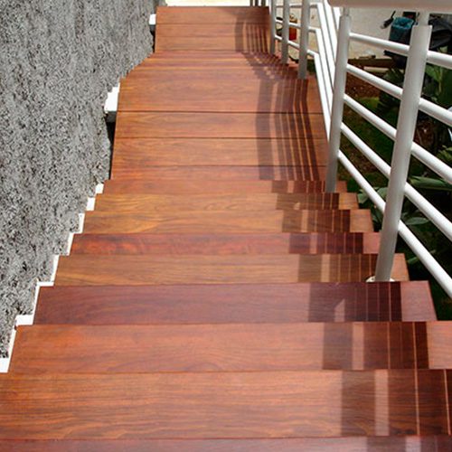 Escada de madeira com degraus lisos e corrimão branco ao lado de uma parede de textura rústica, trazendo um toque natural e elegante ao ambiente.