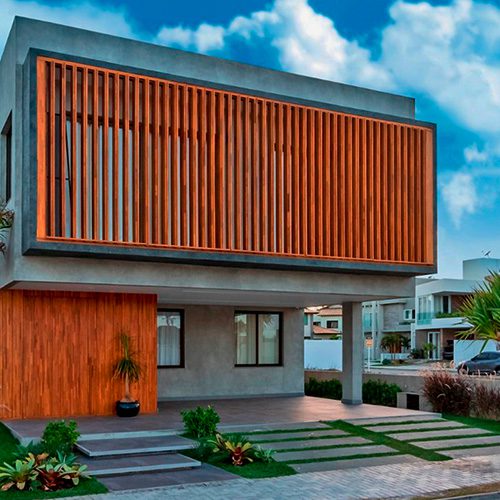 Fachada moderna de casa com brises e painéis de madeira, janelas amplas e jardim na entrada, destacando design arquitetônico contemporâneo.