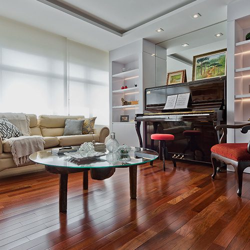 Sala de estar elegante com piso de madeira envernizado, piano preto, sofá claro, mesa de centro em vidro e iluminação natural.