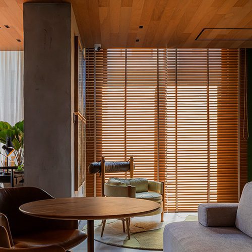 Sala com painéis de madeira, iluminação filtrada por brises e mobiliário elegante, criando ambiente acolhedor e sofisticado.