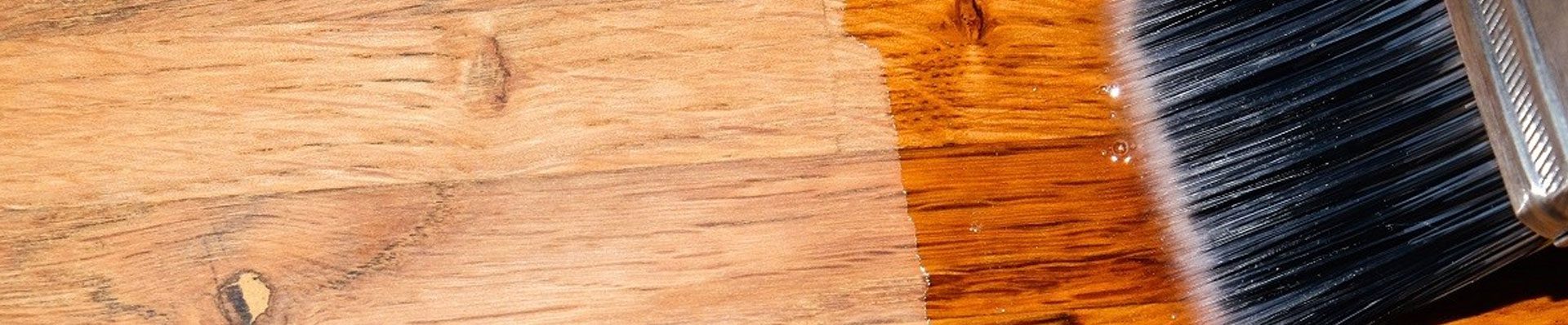 A imagem mostra um piso de madeira com uma parte feita sem manutenção e outra com, e um pincel em cima da parte com manutenção.