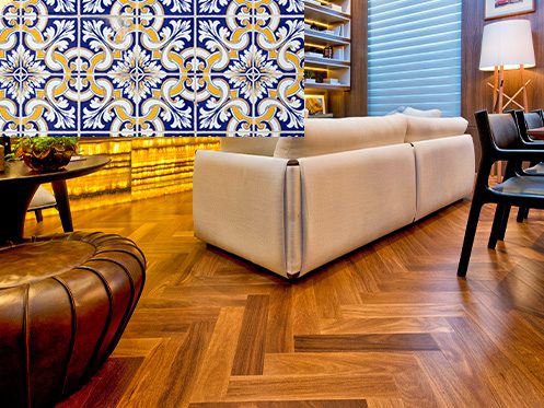 Sala de estar com decoração aconchegante, apresentando piso de madeira em padrão espinha de peixe e parede com azulejos portugueses azuis e amarelos em destaque.