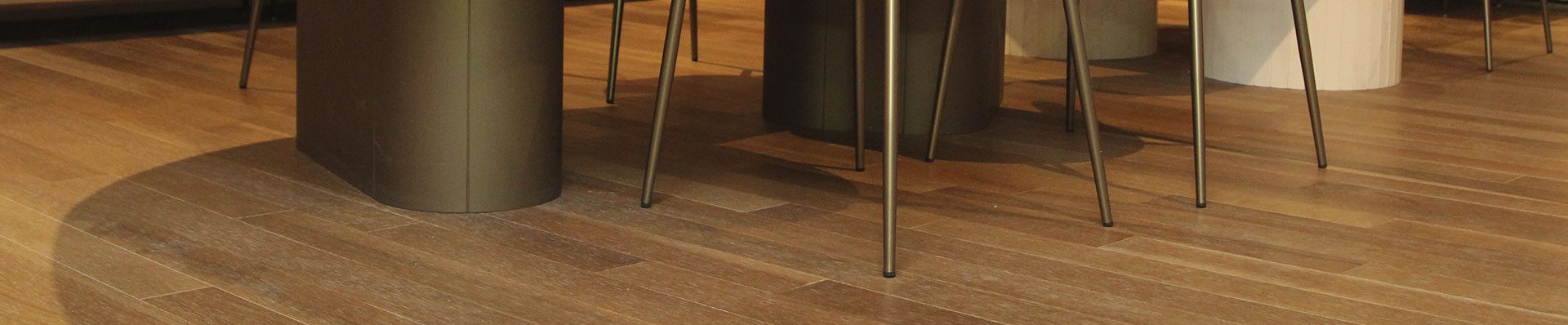 a imagem mostra um ambiente com piso de madeira. No ambiente tem uma mesa oval e duas cadeiras com estofado branco. Nas paredes tem dois espelhos de tamanhos diferentes no formato oval