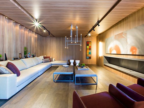 A imagem mostra uma sala de estar com um sofá branco grande, duas mesas de centro e duas poltronas na cor vinha. Do parede oposta do sofá tem um quadro grande e um nicho da mesma largura do quadro