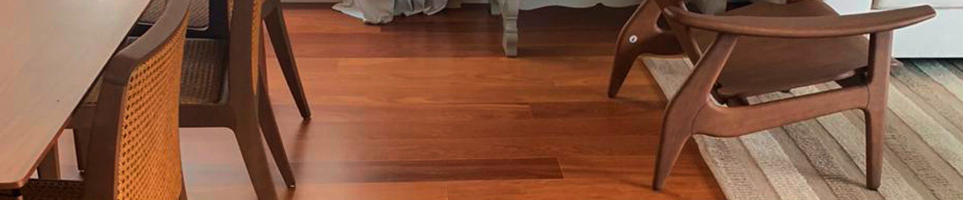 Sala com piso de madeira avermelhada, mesa de jantar, poltronas de design moderno e tapete bege ao lado de sofá claro.