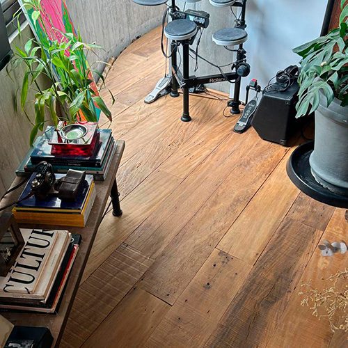 Ambiente com piso de madeira de demolição, decorado com plantas, livros e uma bateria eletrônica, criando um espaço aconchegante e moderno.