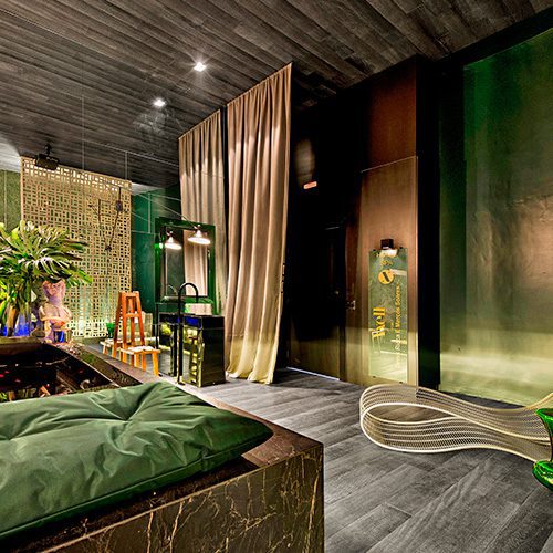 Ambiente sofisticado com piso de madeira escura, cortina de tecido claro, iluminação suave e decoração com plantas e mobiliário moderno.