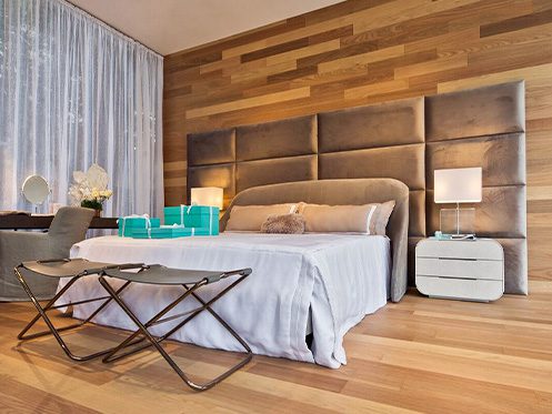 A imagem ilustra um quarto com uma cama de casal e piso de madeira tauari