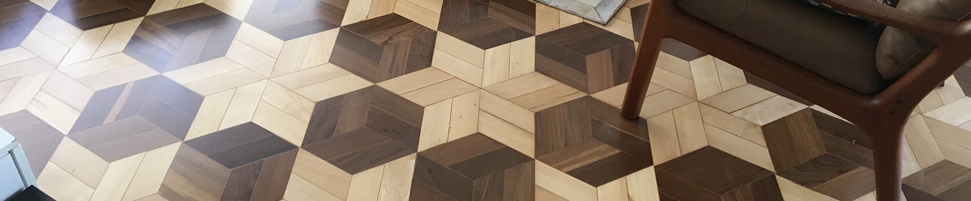 Piso de madeira com padrão geométrico em tons variados, criando um efeito tridimensional, em uma sala de estar com móveis modernos e tapete neutro.