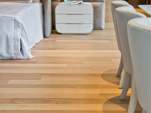 Quarto moderno com piso de madeira clara, cama com roupa de cama branca e cadeiras estofadas, destacando a elegância e aconchego do ambiente.
