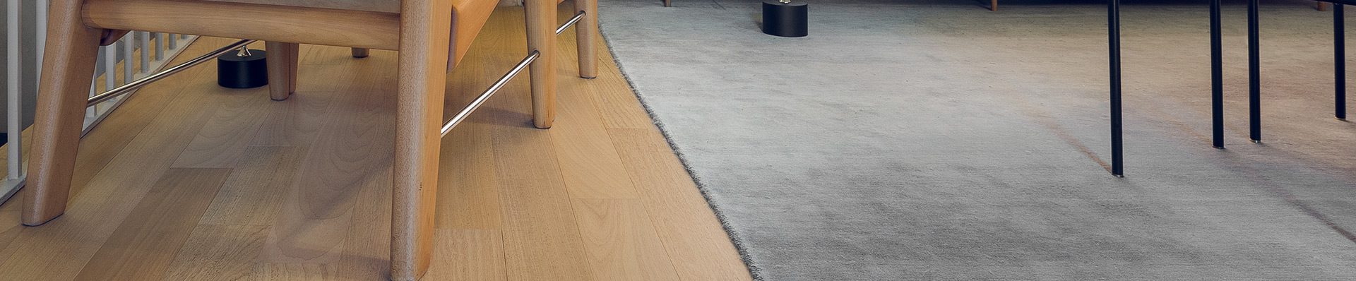 Sala de estar moderna com piso de madeira clara, poltronas de madeira e tecido bege, sofá cinza com almofadas, e mesa lateral com decoração minimalista.