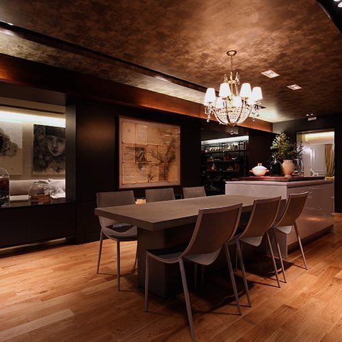 Ambiente interno elegante com piso de madeira teca, mesa de jantar moderna e iluminação quente com lustre central.