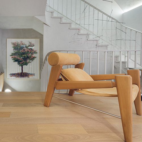 Ambiente moderno com piso de madeira clara, poltrona de design elegante e escada com corrimão metálico. Decoração minimalista e iluminada.