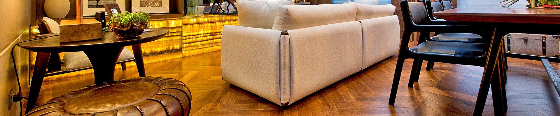 Sala de estar elegante com piso de madeira em padrão espinha de peixe, sofá bege, prateleiras iluminadas com objetos decorativos e uma atmosfera aconchegante.