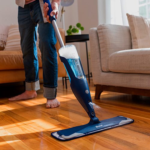 Pessoa limpando piso de madeira com mop em ambiente residencial