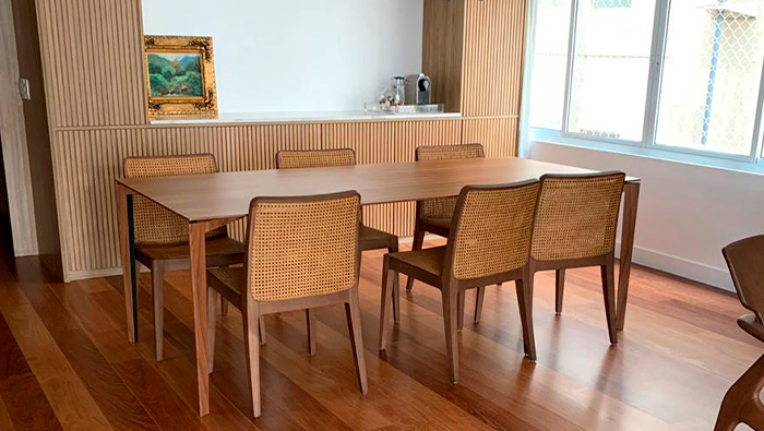 A imagem mostra uma sala de jantar com uma mesa e seis cadeiras e o piso de madeira.