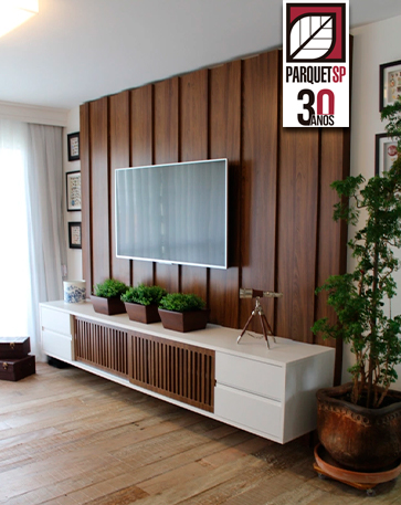 A imagem mostra uma sala com painel de madeira de tv, uma tv pendurada, e um rack.