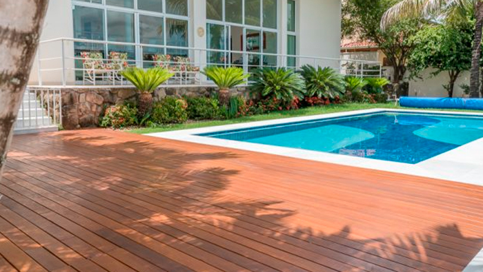 A imagem mostra a area externa de uma casa com um deck de madeira ao redor da piscina.