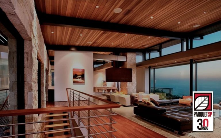 Ao fundo da imagem, há uma sala de estar com forro de madeira.