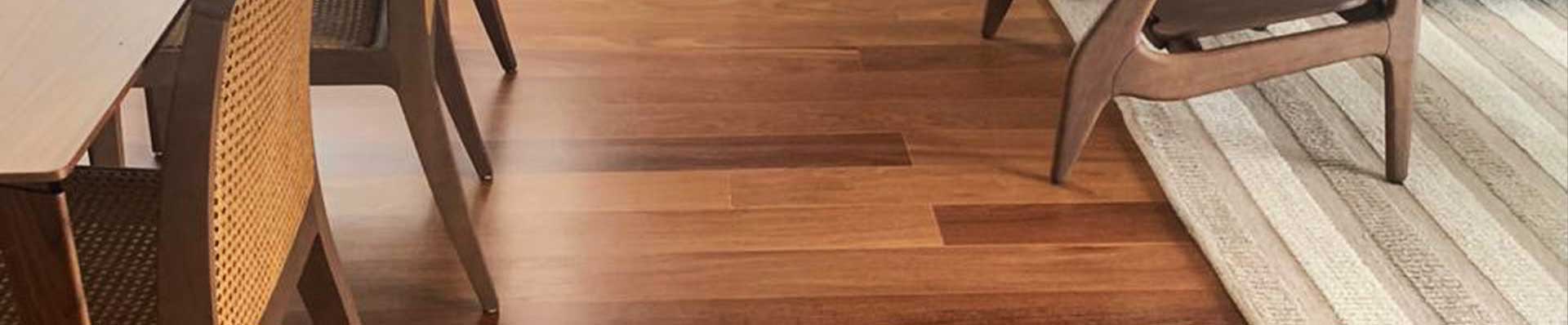 a imagem ilustra um piso de madeira em uma sala, com mesa de jantar e cadeiras à esqueda e tapete e sofá à direita.